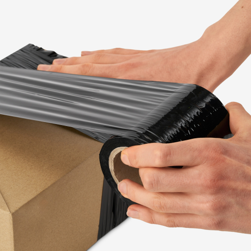 Stretchfolie in der Anwendung. Eine Männerhand wickelt die Folie manuell um einen Karton. Die Folie reißt nicht