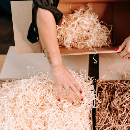Person greift nach Holzwolle, die zum Schutz von Paketen verwendet wird.