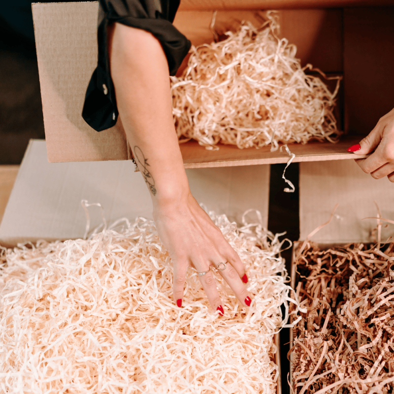 Person greift nach Holzwolle, die zum Schutz von Paketen verwendet wird.