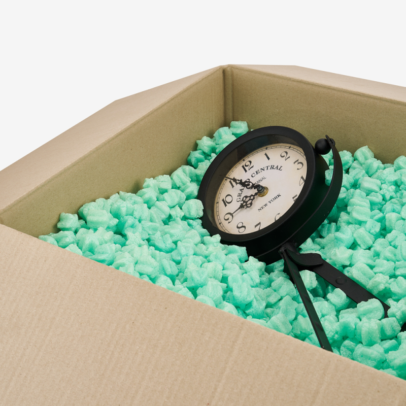 Verpackter Wanduhr in einem Karton, gesichert mit grünem Skropak in Sternchenform.