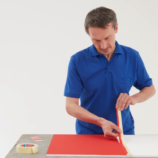 Abziehen des Papier-Abdeckbands tesa® 4323 durch einen Mitarbeiter von der gestrichenen Oberfläche.